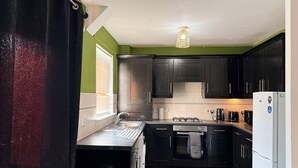Une cuisine de taille réduite, avec des meubles de couleur sombre, un évier en acier inoxydable, une cuisinière à gaz et un réfrigérateur blanc.