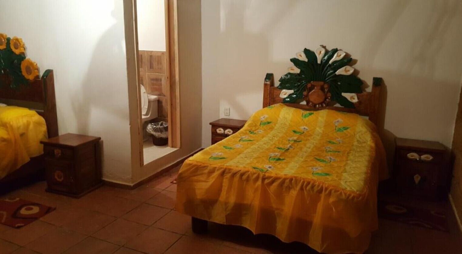 Une chambre à coucher comprenant un lit, des tables de chevet, une tête de lit en bois et une porte donnant sur une salle de bain.