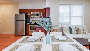 A modern kitchen with stainless steel appliances, a dining area with a table set for four, and a cozy living area with a sofa and decorative pillows. - The Pennside 2BR Stay (Philadelphia)