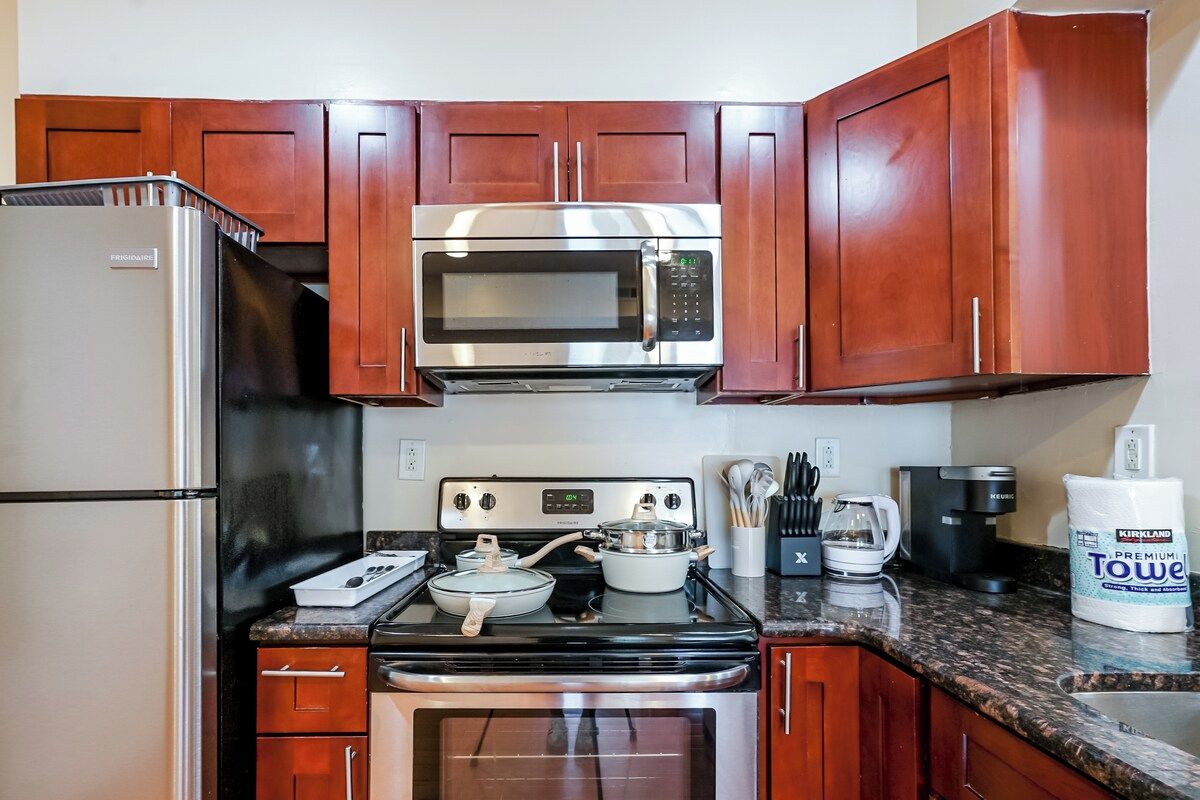 A compact kitchen with a stainless steel refrigerator, a microwave, a stove, and a coffee maker.