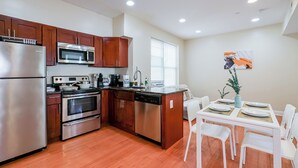 A modern kitchen with stainless steel appliances, wooden cabinets, and a dining area with white chairs. - The Pennside 2BR Stay (Philadelphia)