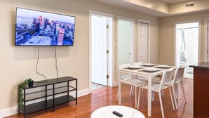 A modern living room with a flat-screen TV, a dining table with chairs, a white coffee table, and a black console table with a plant. - The Pennside 2BR Stay (Philadelphia)