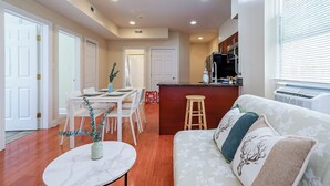 A modern kitchen with a central island, a dining area with white chairs, and a living room with a sofa and decorative pillows. - The Pennside 2BR Stay (Philadelphia)