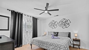 Une chambre à coucher comprenant un lit, un ventilateur de plafond, une table de chevet, une lampe et un mur orné d’œuvres d’art géométriques.