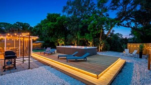 Une terrasse dotée de chaises longues, d’un jacuzzi et d’un espace clos par des parois de verre, agrémenté de guirlandes lumineuses.