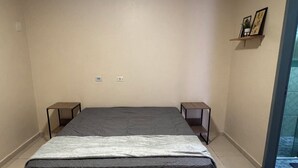 A bedroom with a bed, two bedside tables, a small shelf with pictures, and a door leading to a balcony.