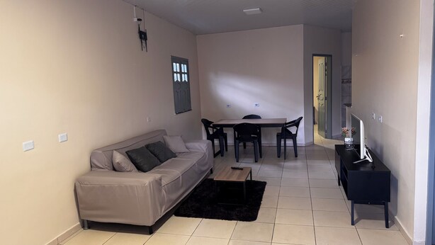 A living room with a sofa, a coffee table, a TV stand, and a dining area with a table and chairs.