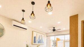Un comedor moderno con una mesa de madera y sillas azul oscuro, un ventilador de techo y lámparas colgantes.