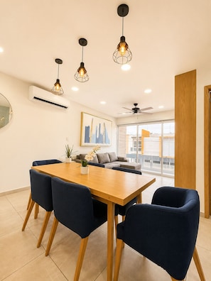 A modern dining area with a wooden table and dark blue chairs, a ceiling fan, and pendant lights.