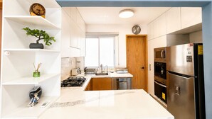 Una cocina moderna con armarios blancos, encimera de mármol, horno empotrado y refrigerador de acero inoxidable.