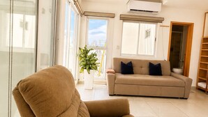 Una sala de estar con un sofá, una silla, una planta en maceta y un ventanal corredero.