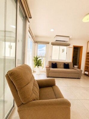 A living room with a sofa, a chair, a potted plant, and a sliding glass door.