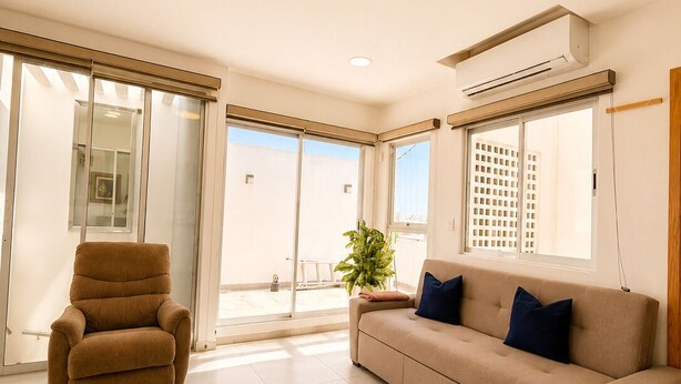 Una sala de estar con un sofá, un sillón reclinable y un ventanal corredizo que da a un área exterior.