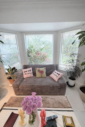 Un rincón acogedor con una zona de estar acolchada, un jarrón de flores y un control remoto sobre una mesa.