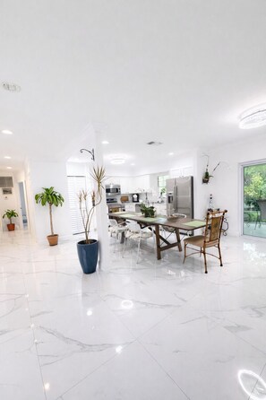 Una cocina moderna con armarios blancos, electrodomésticos de acero inoxidable y un comedor con piso de mármol.
