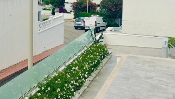 A residential area with a clear view of the sea, a white building with a balcony, and a parked car. - Giardino dei Trulli Villa al Mare (Capitolo)
