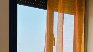 A window with a sheer curtain, a clear view of buildings and a body of water outside. - Giardino dei Trulli Villa al Mare (Capitolo)