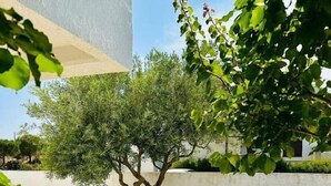 An outdoor patio with white chairs and a lounge chair, surrounded by a low wall and a tree. - Giardino dei Trulli Villa al Mare (Capitolo)