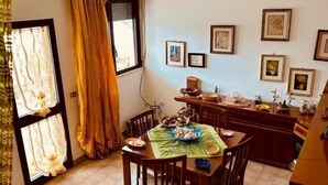 A dining area with a table set for four, a window with curtains, and framed pictures on the wall. - Giardino dei Trulli Villa al Mare (Capitolo)