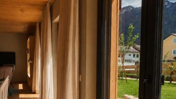 Ein Zimmer mit Holzboden, großen Schiebeg lass türen und Blick auf eine Berglandschaft.