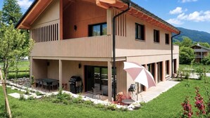 Ein zweistöckiges Haus mit überdachter Terrasse, Grill und Garten.