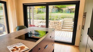 Eine moderne Küche mit Einbauherd, einer Zeitschrift auf der Arbeitsplatte und Blick in den Garten durch Glastüren.