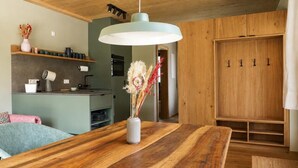Una mesa de comedor de madera con un jarrón de flores secas, una lámpara colgante y una cocina con encimera verde y armarios de madera.
