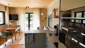 Una cocina moderna con horno empotrado, un comedor con mesa y sillas de madera, y un ventanal con cortinas.