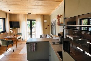A modern kitchen with a built-in oven, a dining area with a wooden table and chairs, and a large window with curtains.