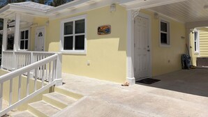 A two-story house with a porch, a front door, and a staircase leading to the upper level. - Golden Hour: - BRAND NEW 2026 - sunsets, beach, and park in perfect proximity. (Spanish Wells)