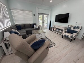 A modern living room with a sectional sofa, a coffee table, a TV, and a patterned armchair. - Golden Hour: - BRAND NEW 2026 - sunsets, beach, and park in perfect proximity. (Spanish Wells)