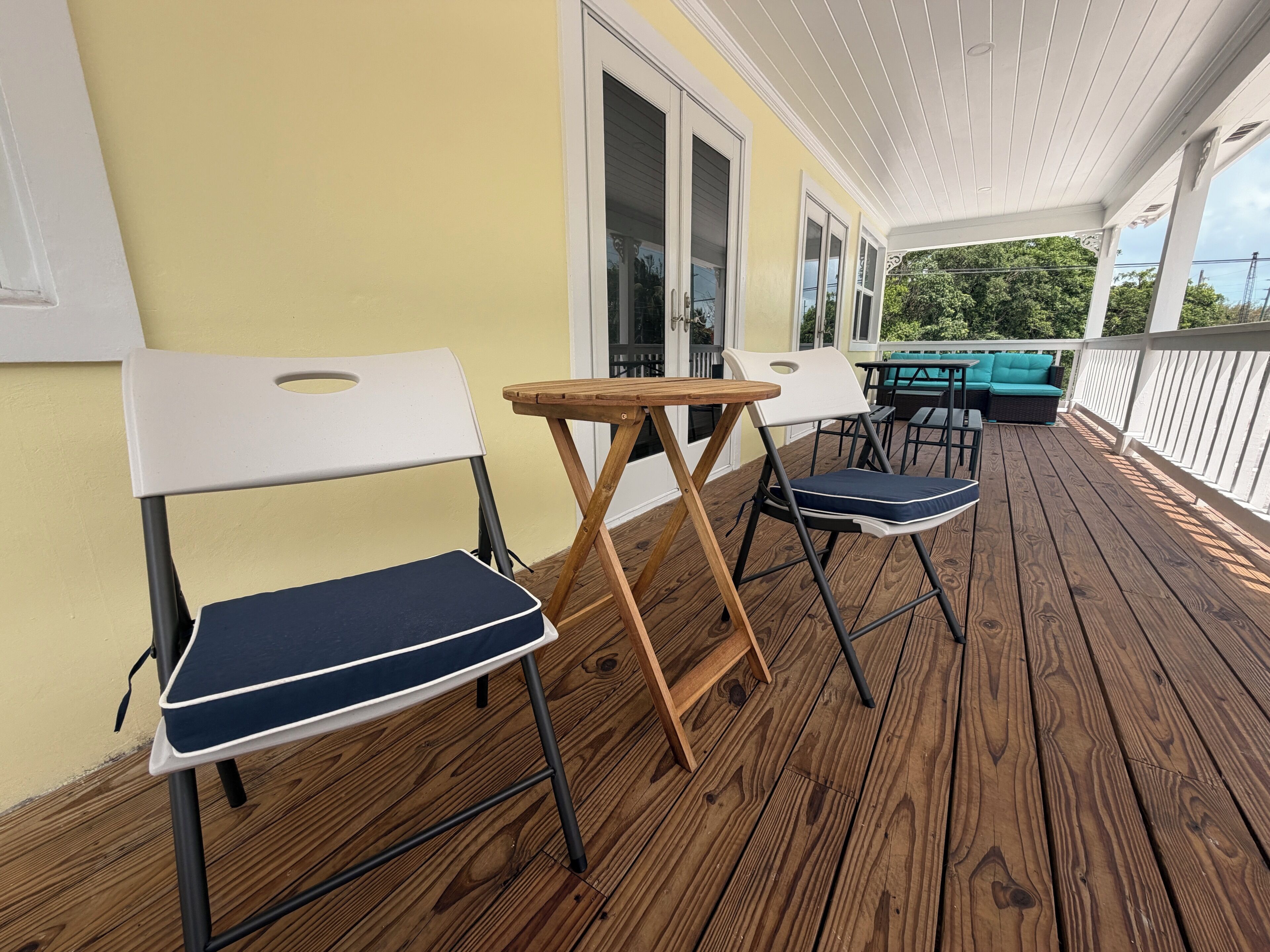 Eine überdachte Terrasse im Freien mit Holzboden, weißen Geländern und zwei Klappstühlen.
