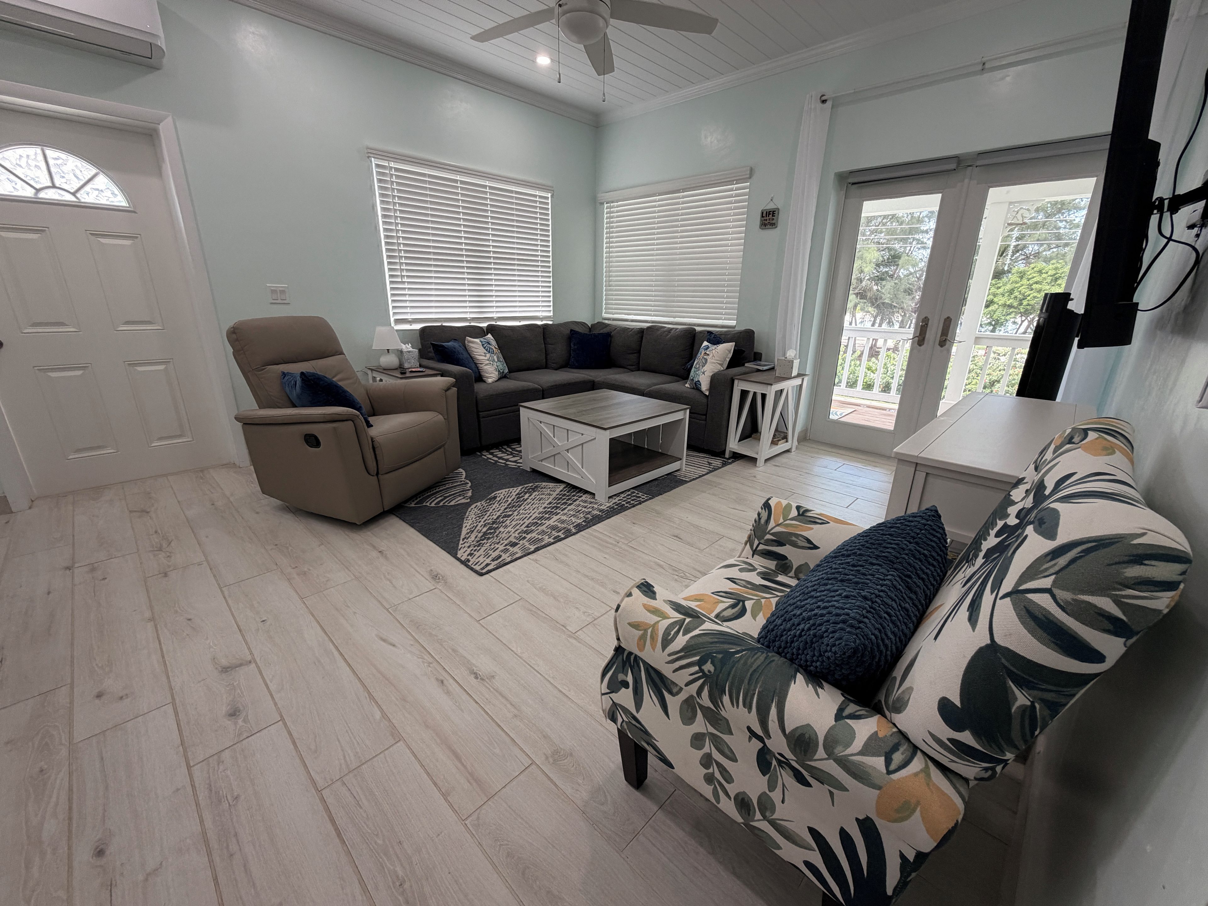 A living room with a sofa, armchair, coffee table, and a view through the glass door.
