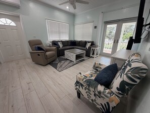 A living room with a sofa, armchair, coffee table, and a view through the glass door. - Golden Hour: - BRAND NEW 2026 - sunsets, beach, and park in perfect proximity. (Spanish Wells)