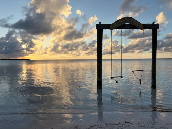 A swing set over a calm body of water with a sunset in the background.