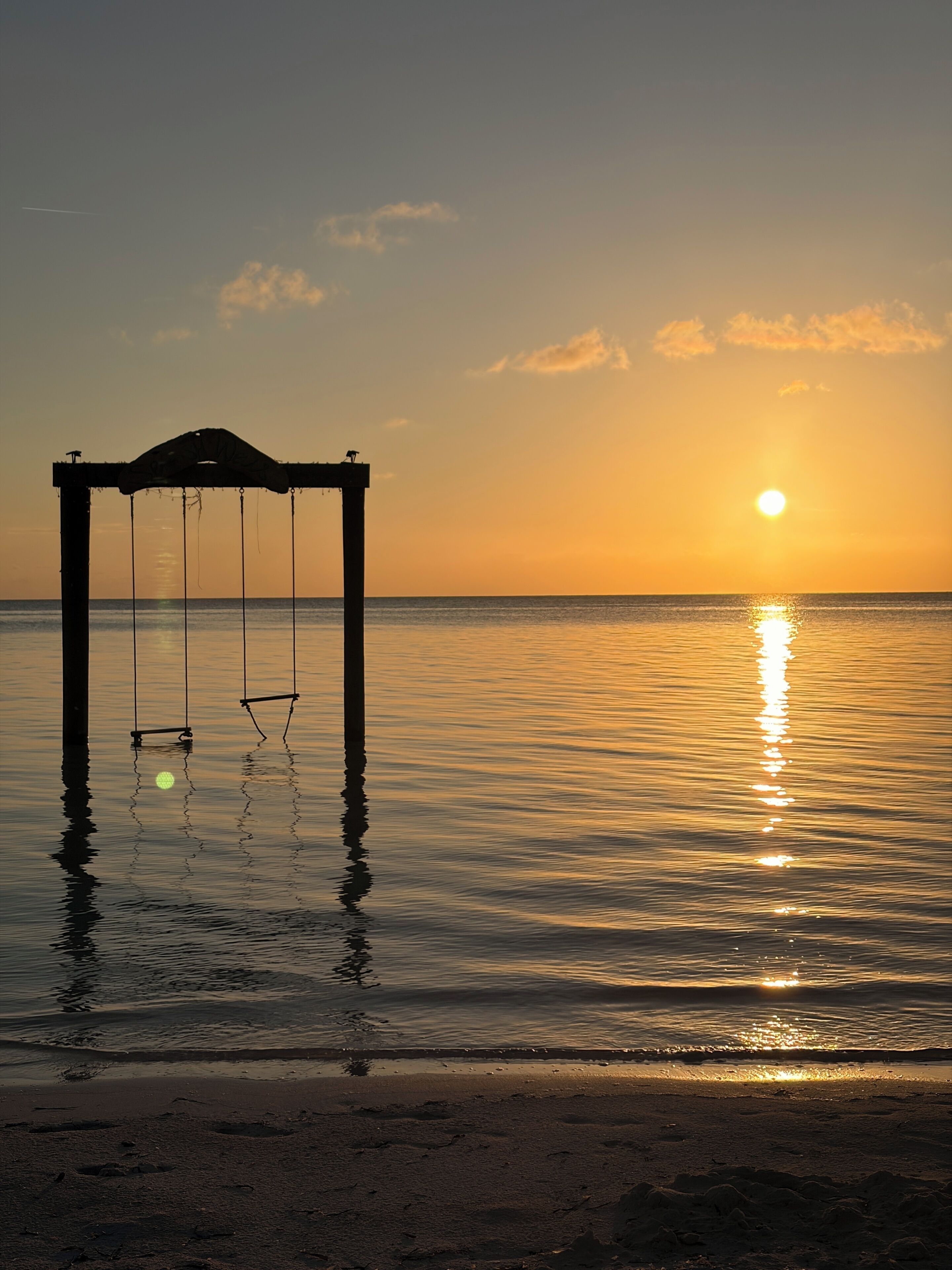 A swing set over water at sunset.