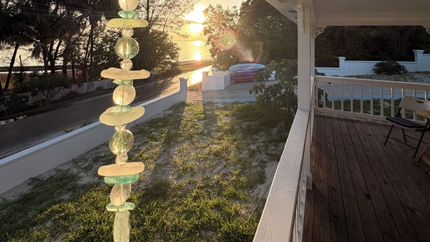 A wooden deck with a railing, a hanging decorative object, and a view of the sunset. - Golden Hour: - BRAND NEW 2026 - sunsets, beach, and park in perfect proximity. (Spanish Wells)