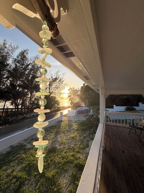 A wooden deck with a railing, a hanging decorative object, and a view of the sunset.