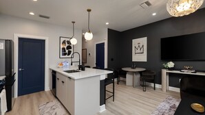 A modern kitchen with a central island, a dining area with a round table, and a living space with a black sofa and a TV mounted on the wall. - Luxe Modern Artsy TH in Tampa Heights/Next to Downtown/Everything You Need (Tampa)
