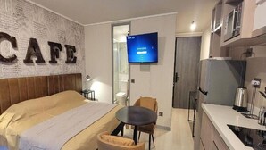 Ein Hotelzimmer mit einem Bett, einem kleinen runden Tisch, einem Sessel, einem Fernseher und einer Küchenzeile.