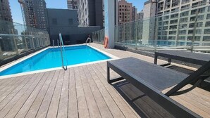 Ein Pool auf dem Dach mit Holzterrasse, Glasgeländern und einer Sitzbank.