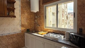 A kitchen with a built-in stove, a sink, a window with a view of buildings, and a ceiling light fixture. - Cozy 2-bedroom apartment in Tanger city center (Tanger)