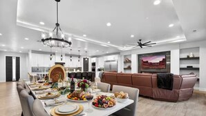 Un espace de salle à manger moderne, avec une longue table dressée pour un repas, un ventilateur de plafond et une grande fenêtre donnant sur le paysage urbain.