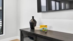 Une pièce moderne avec une console en bois foncé, un téléviseur à écran plat fixé au mur et une fenêtre équipée de stores.