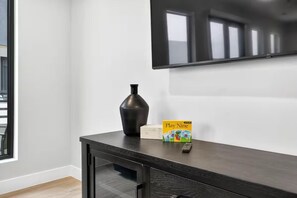 Ein modernes Zimmer mit einer dunklen Holztruhe, einem an der Wand montierten Flachbildfernseher und einem Fenster mit Jalousien.