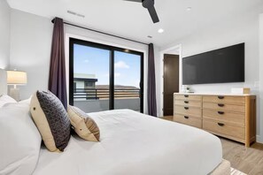 Ein modernes Hotelzimmer mit einem großen Bett, einem Flachbildfernseher, einer Holzkommode und einem Balkon mit Blick.