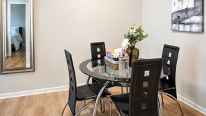 Comedor con una mesa redonda de vidrio, cuatro sillas negras, un florero con flores y un cuadro en la pared.