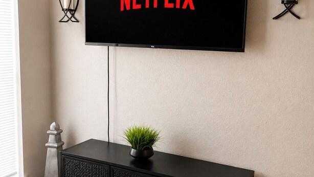 Una sala moderna con un televisor montado que muestra 'NETFLIX', una consola negra con una planta y apliques decorativos en la pared.