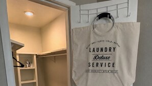 Una bolsa para lavandería colgada en una puerta, un armario blanco con estantes y un suelo de madera.