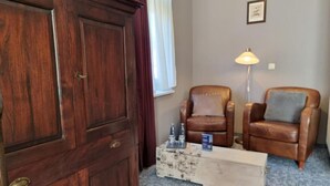 Una habitación con un armario de madera, dos sillones de cuero, una mesita de café y una lámpara de pie.